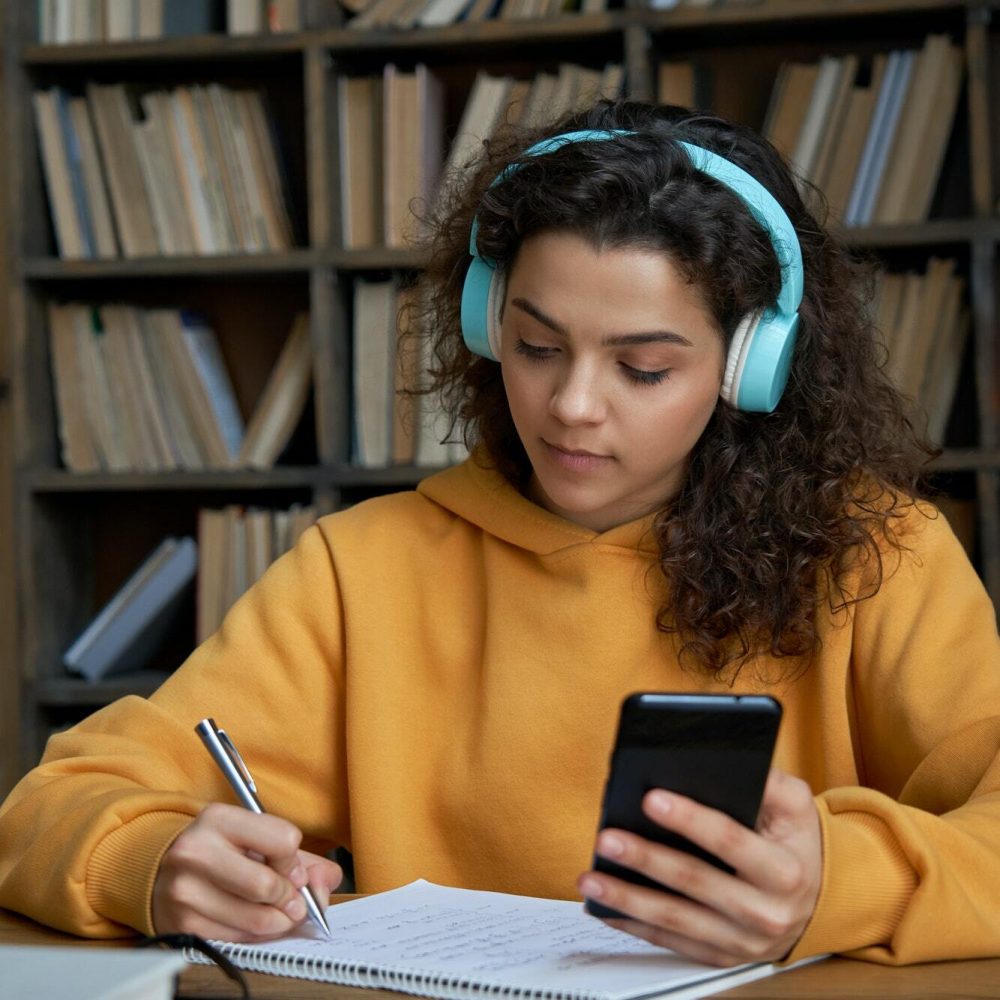 Hispanic teen girl wear headphones hold phone distance learning in mobile app.
